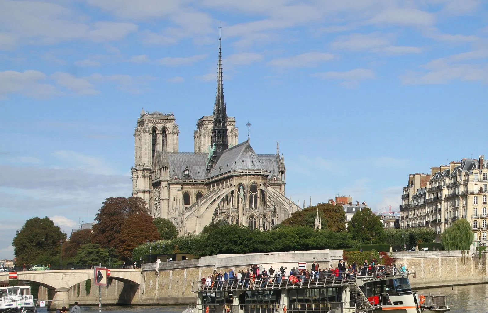 La cattedrale di Notre-Dame de Paris vista dal lungosenna, con un battello turistico sul fiume e gli alberi dell'Île de la Cité